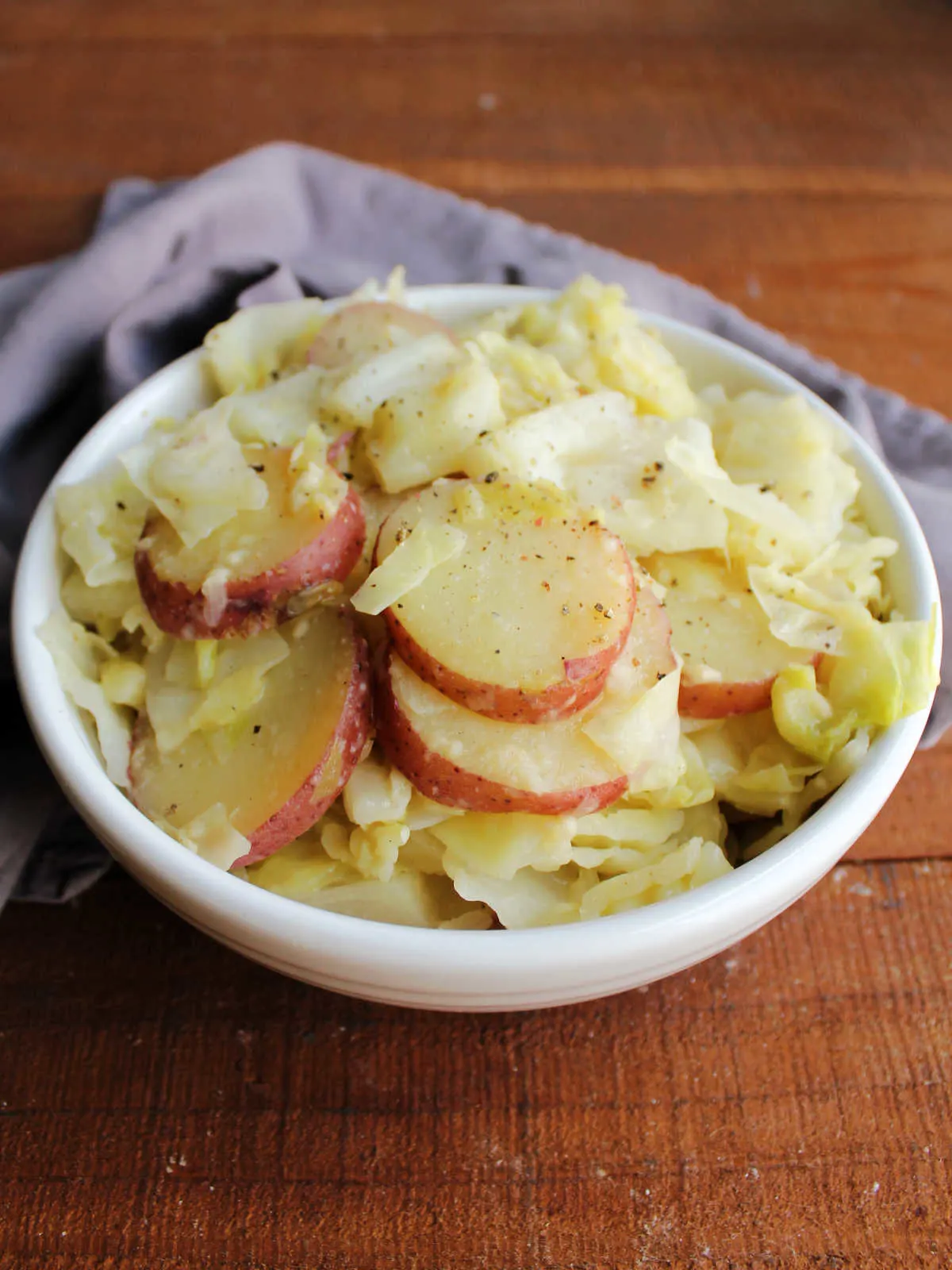 Serving bowl filled with cooked cabbage and potatoes topped with Parmesan cheese and ground black pepper.
