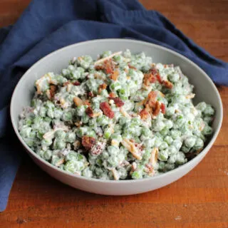 Serving bowl filled with creamy pea salad with creamy dressing, cheese and crumbled bacon.