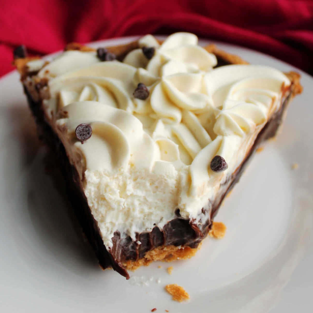 Slice of chocolate pie with smooth chocolate filling and swirls of cream cheese whipped cream piped on top missing bite in front showing the layers.
