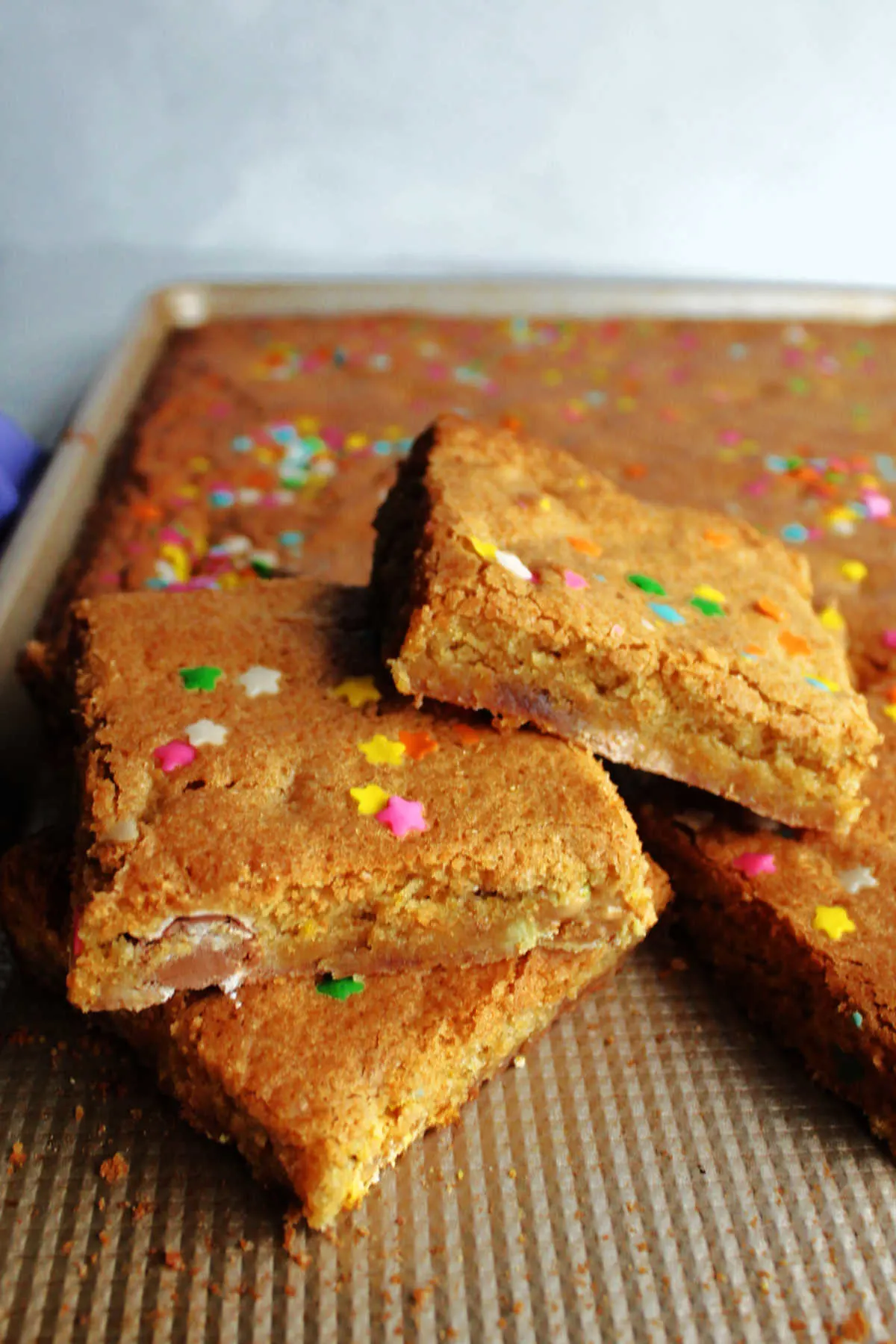 pan of blondies fresh from the oven, dotted with flower sprinkles and filled with candy eggs with pieces cut and stacked.