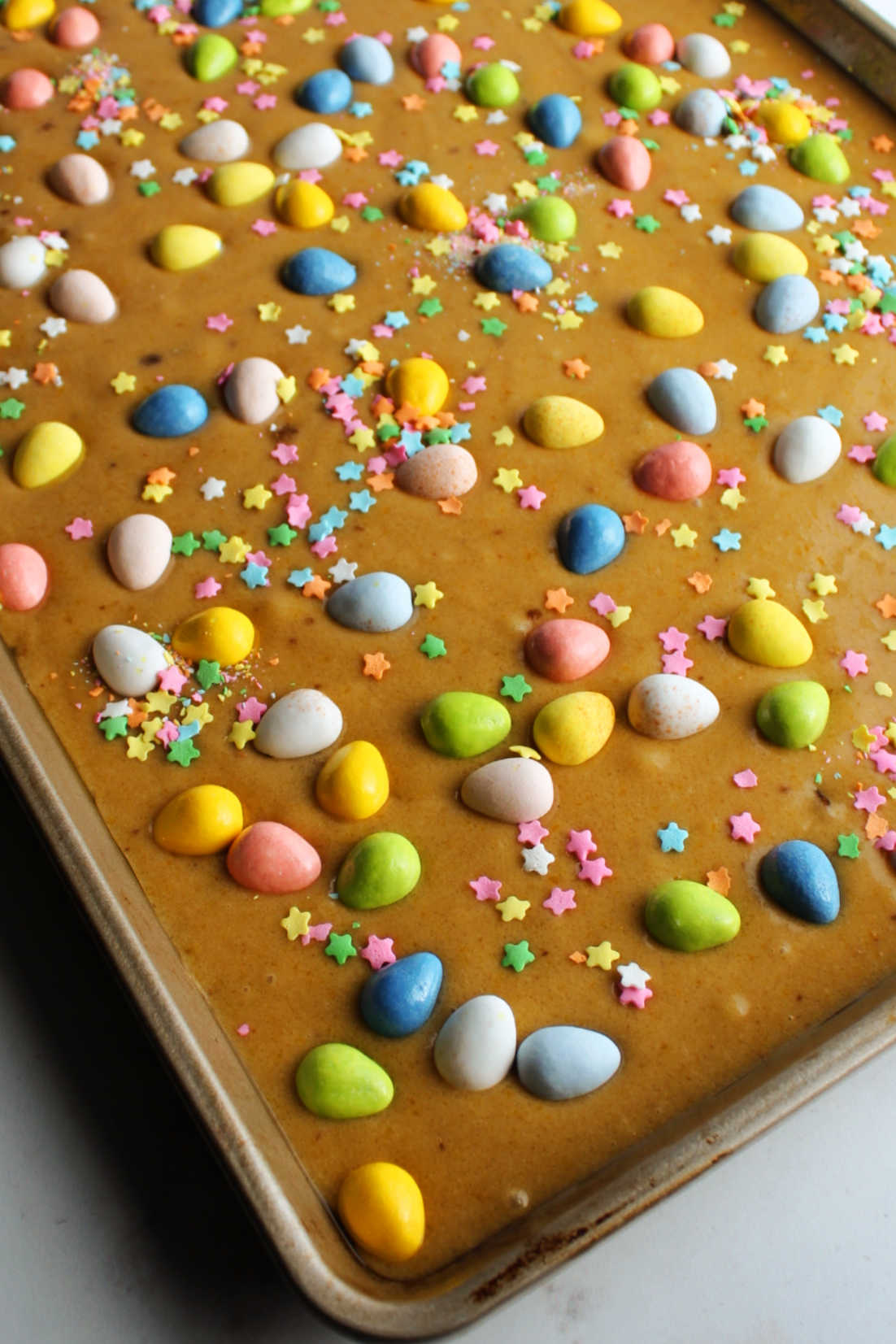 sheet pan filled with blondie batter topped with candy eggs and spring sprinkles.