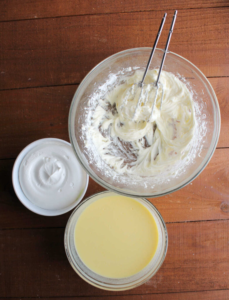 bowl of cream cheese mixture, bowl of pudding mixture and container of whipped topping ready to be mixed together into pudding layer for dirt pudding.