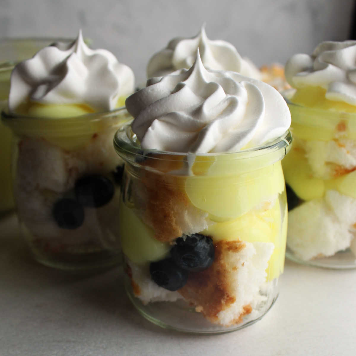 Small glass jars filled with layers of angel food cake, blueberries, lemon yogurt mixture and topped with whipped cream.