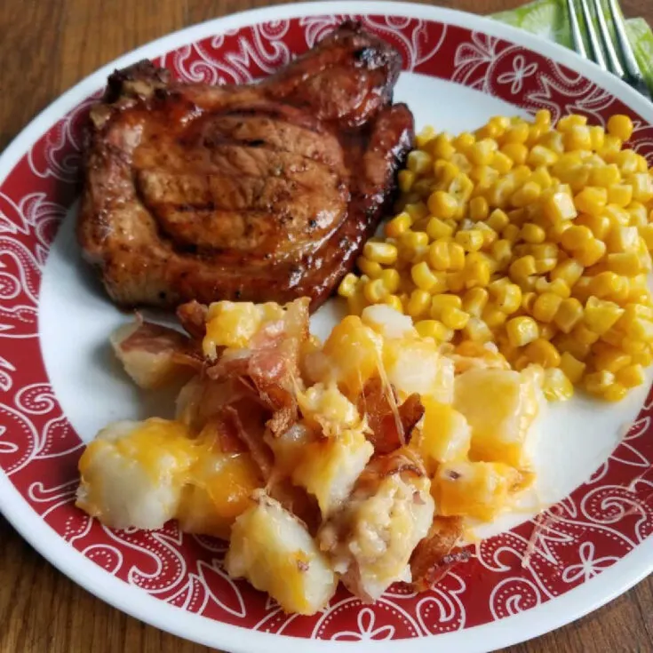 plate of BBQ pork chops, corn and potatoes with cheese and bacon.