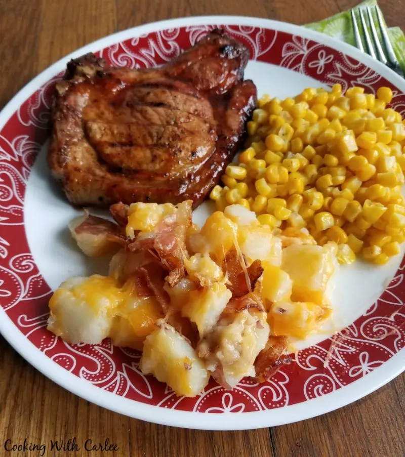 Plate of cheesy potatoes with bacon, bbq pork chop and corn ready to eat.