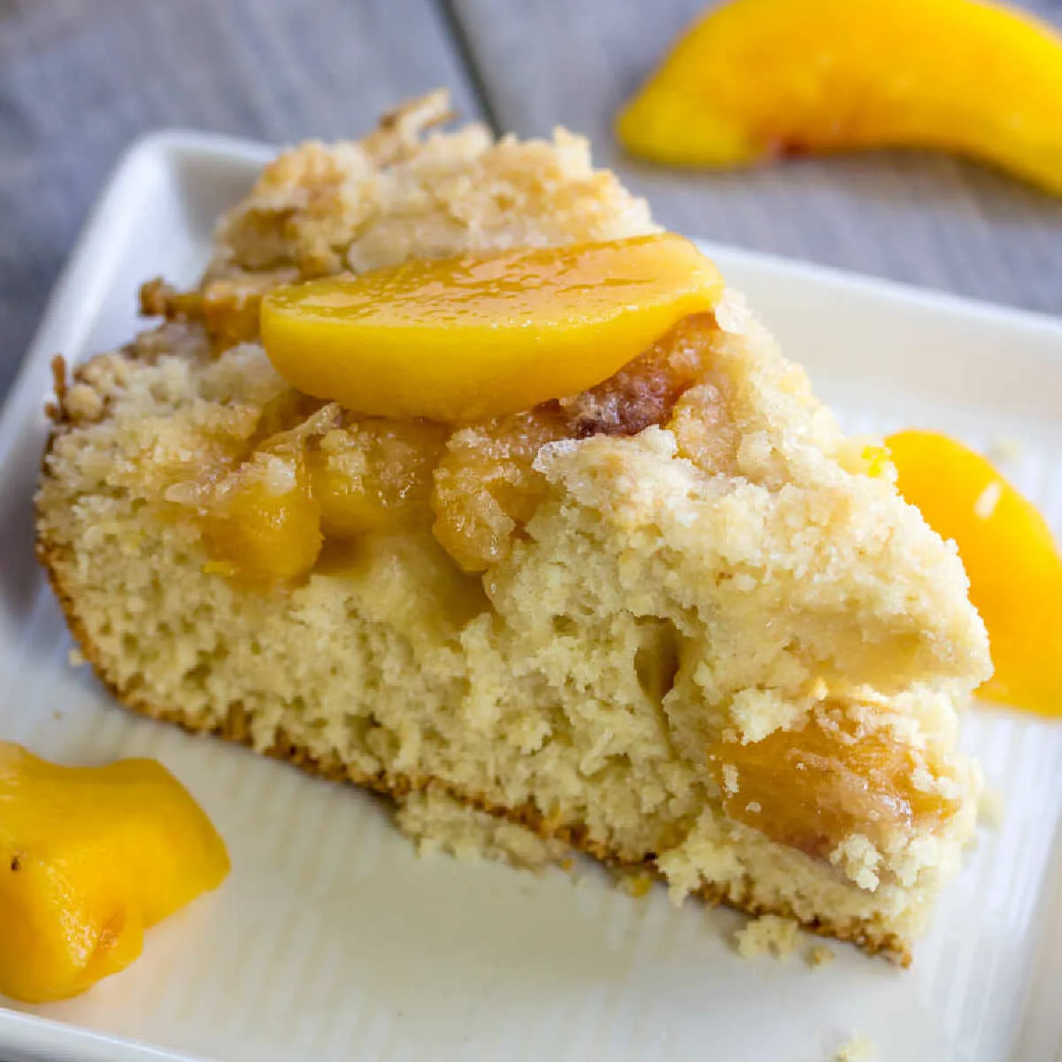 Slice of peach coffee cake with crumb topping served with extra peach slices.