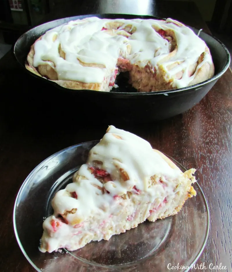 slice of strawberry cinnamon roll with large cast iron skillet behind it.