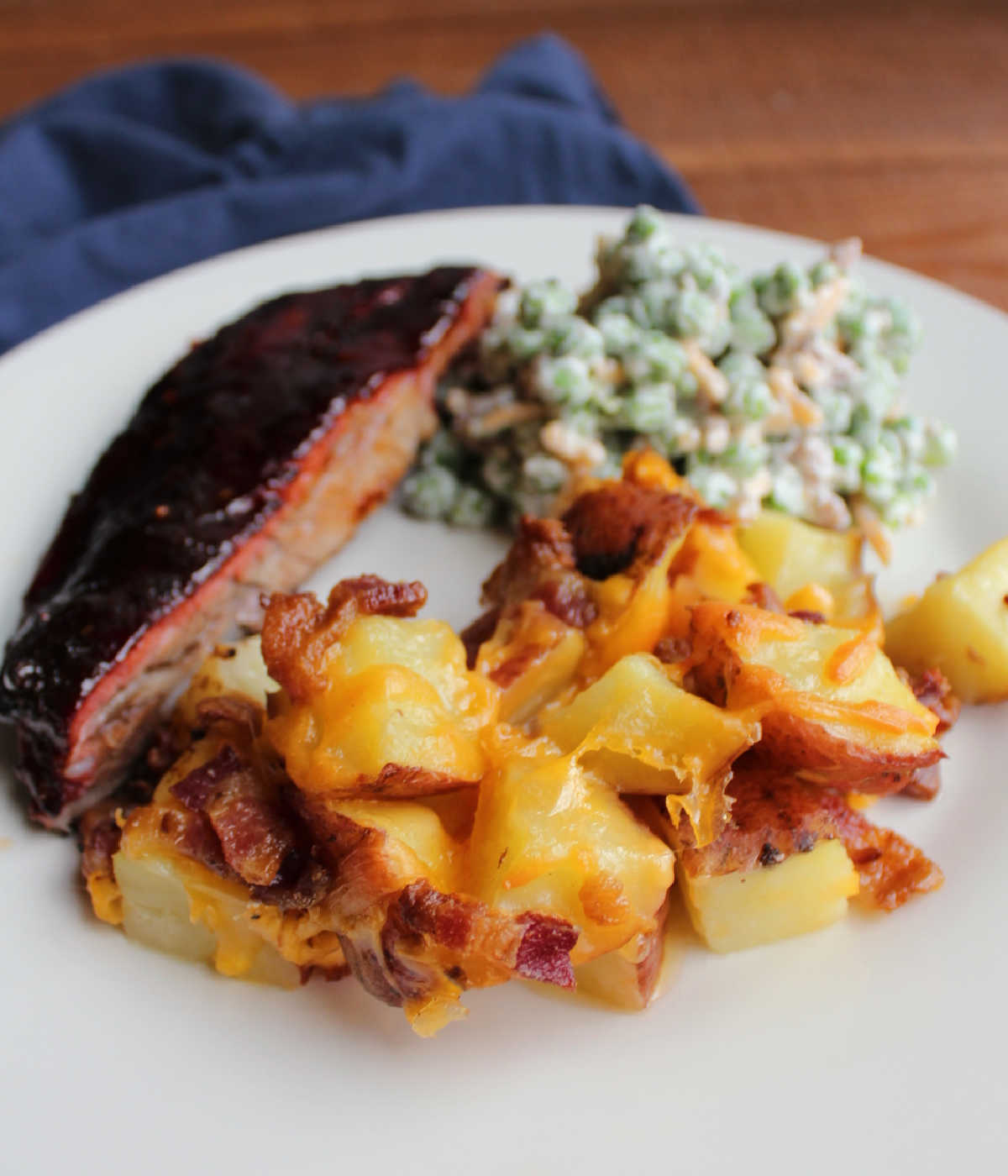 Serving of potato casserole with cheese and bacon on plate with bbq ribs and some pea salad. 
