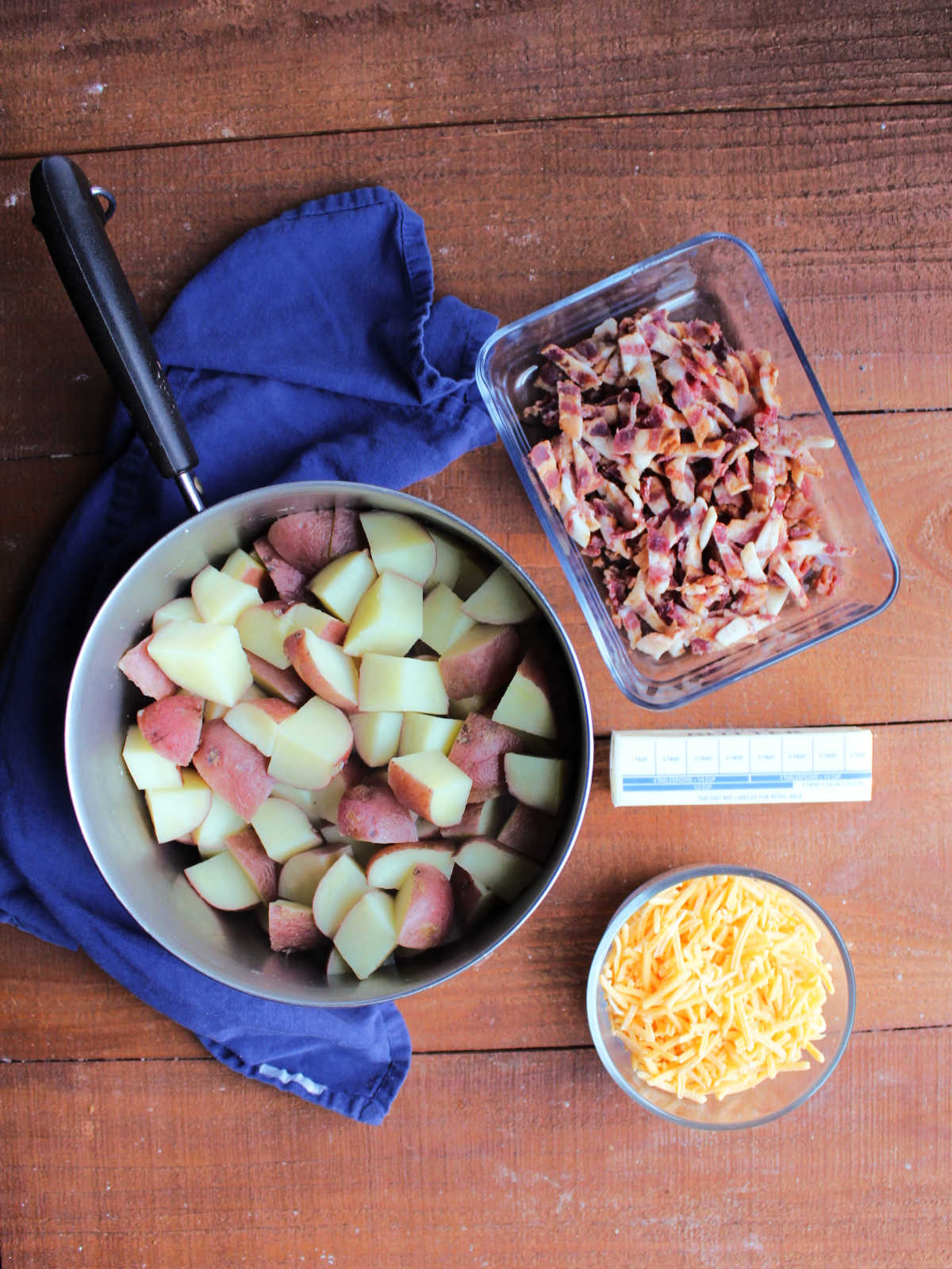 Ingredients including shredded cheddar, butter, chopped bacon and boiled chunks of potatoes. 