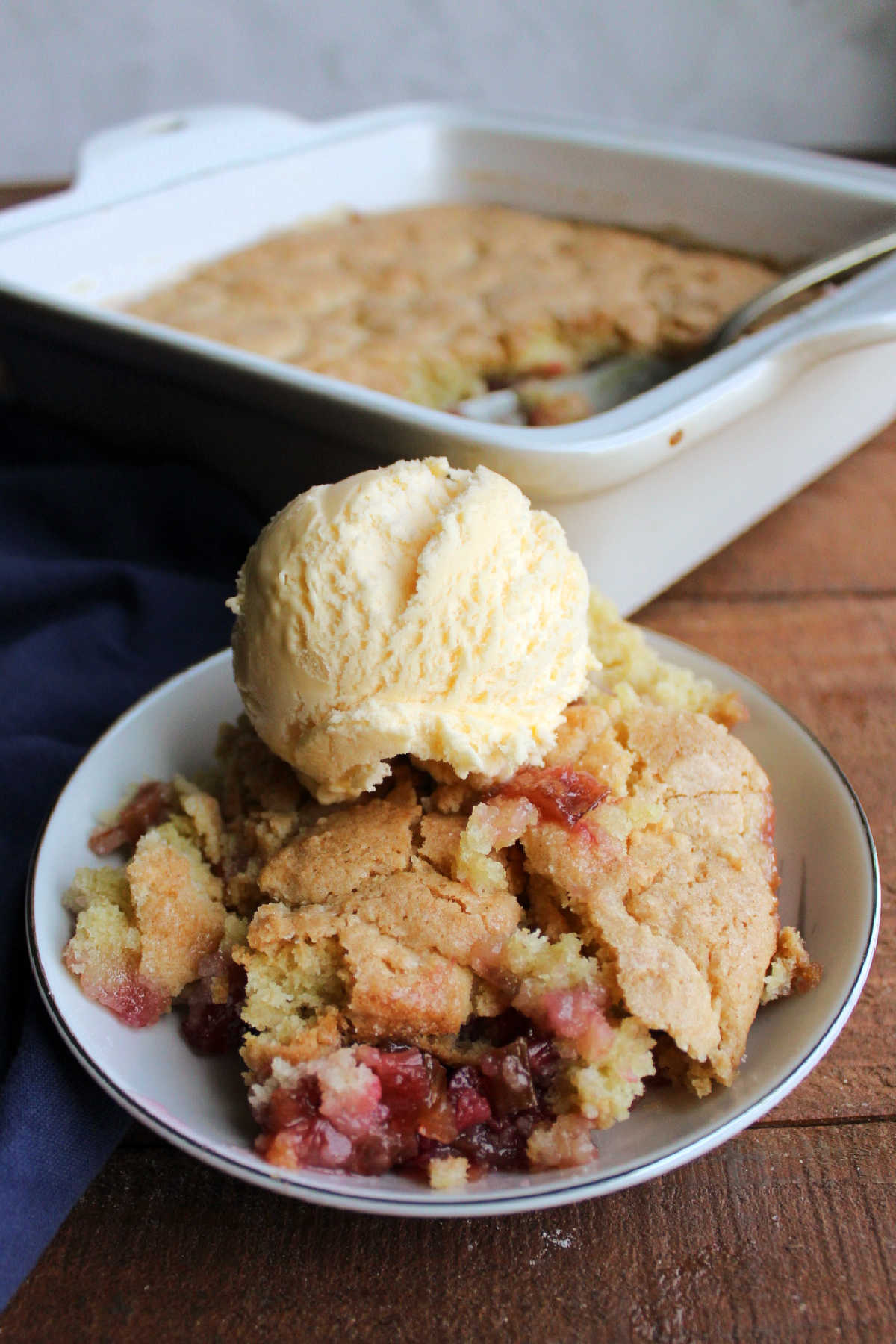 Serving of sweet biscuit topped rhubarb cobbler topped with scoop of vanilla ice cream. 