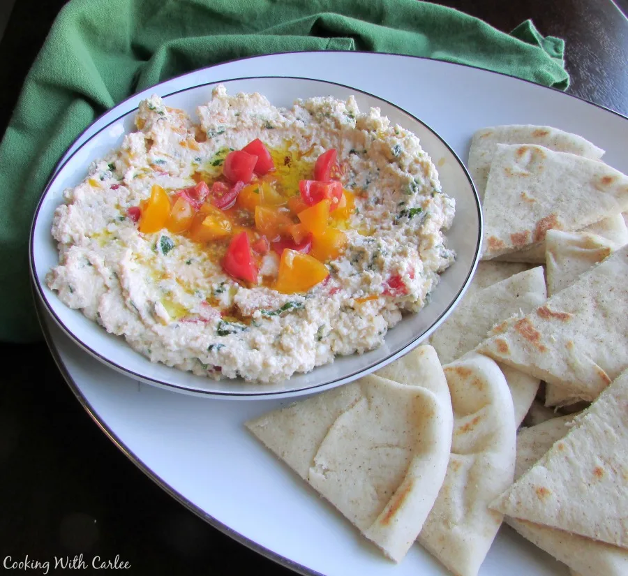 Bowl of Egyptian feta spread with herbs and tomatoes on platter with wedges of pita bread.