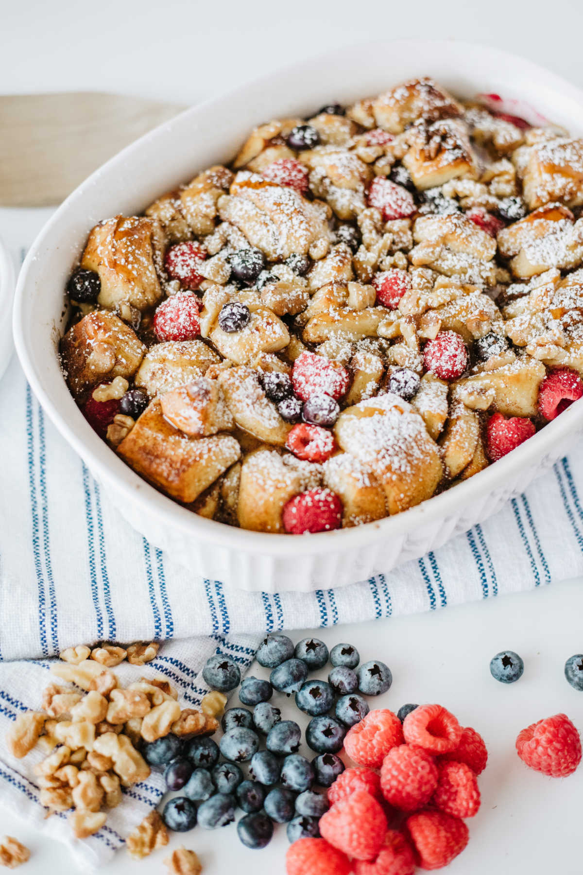 Cinnamon roll french toast casserole with berries and powdered sugar, ready to eat.