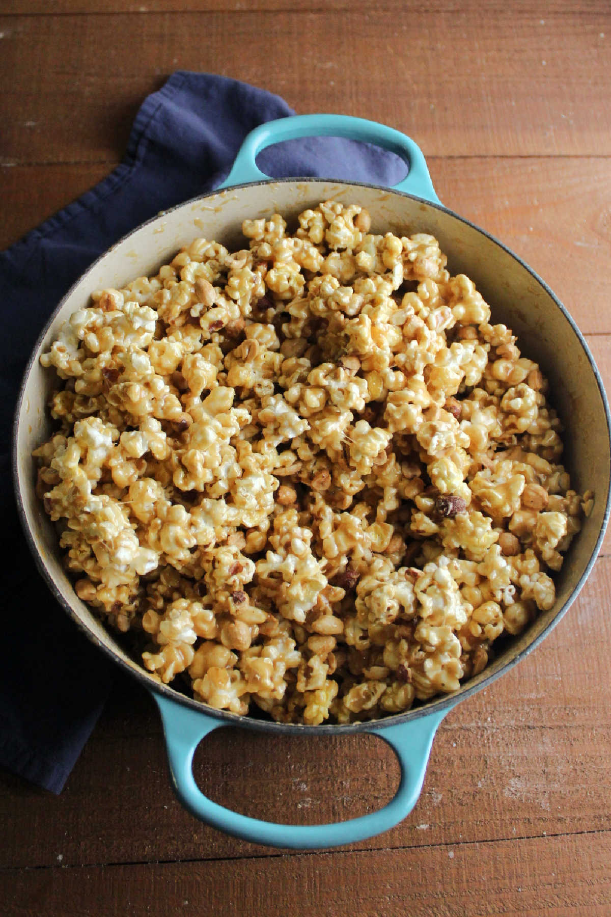 Dutch oven filled with popcorn and peanuts coated in chewy caramel mixture, ready to be spread out on baking pans to go in the oven.