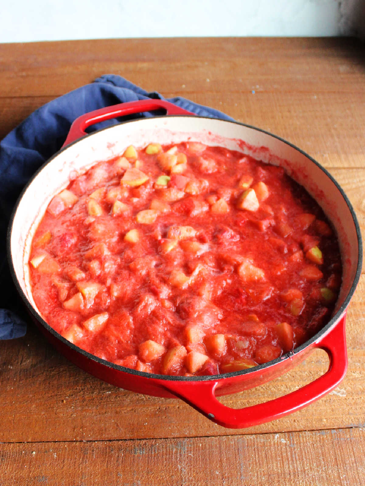 Pan of cooked fruit mixture showing softened apple chunks in mushy rhubarb and strawberry mixture.