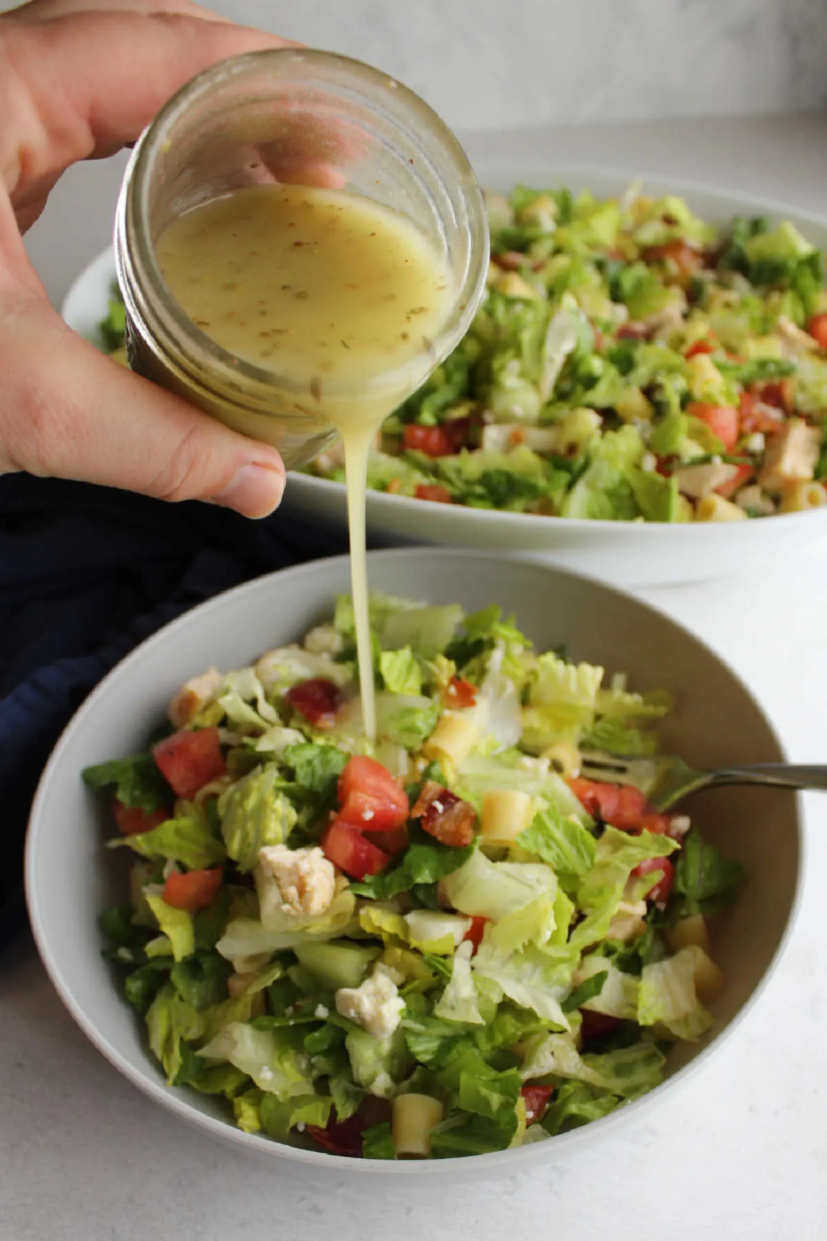 Pouring salad dressing over small bowl of chopped salad.