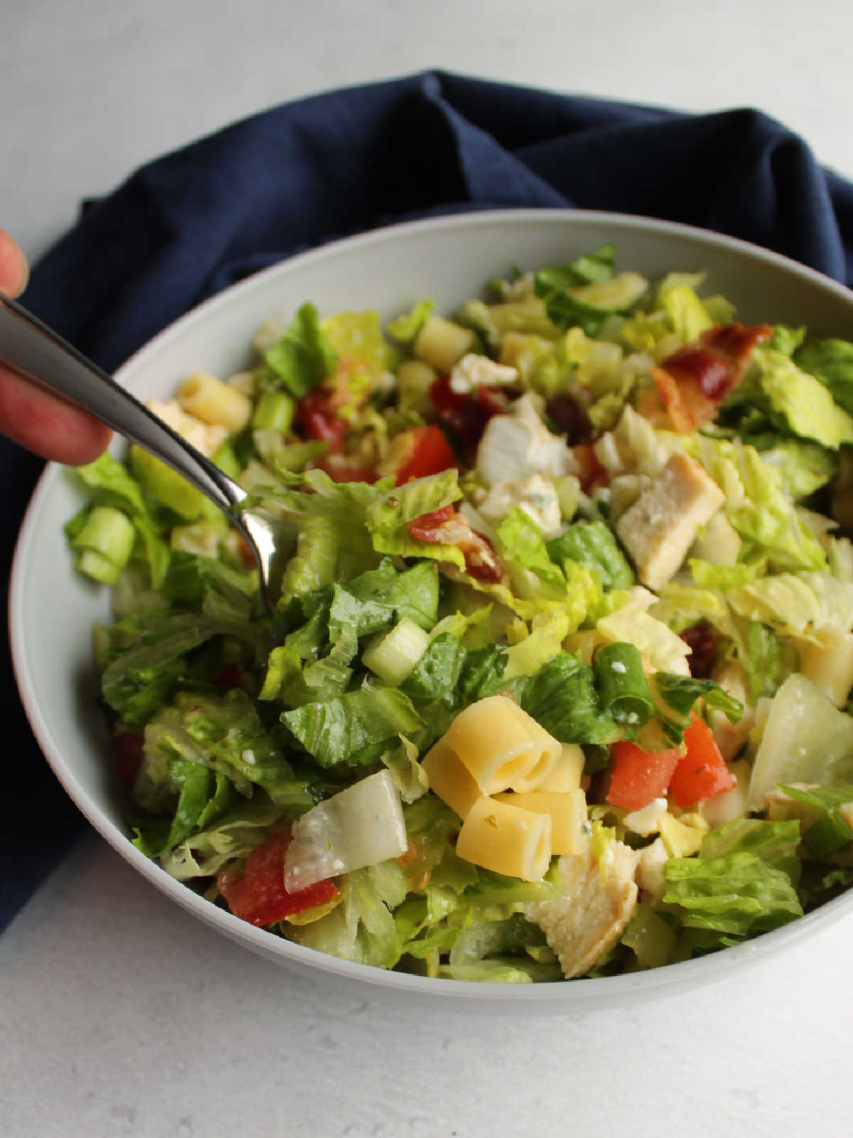 Portillo's Style Chopped Salad 6 Fork getting a bite of chopped salad out of a bowl showing greens, pasta, chicken, cheese, tomatoes and more.