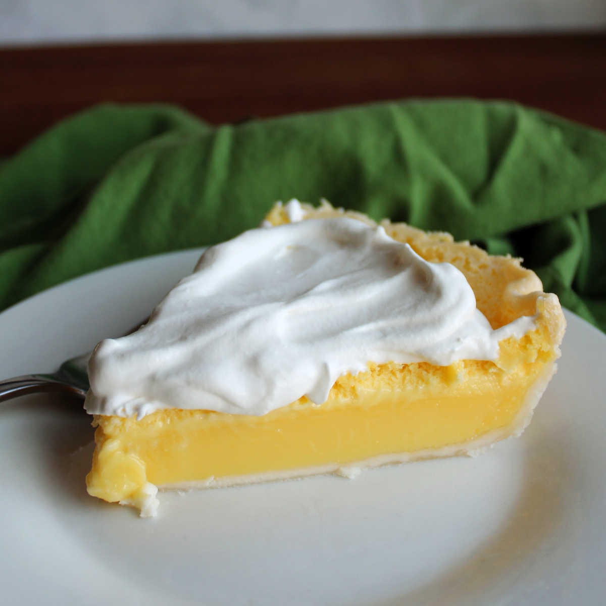 Side view of slice of lemon pie showing smooth lemon filling topped with fluffy white honey whipped cream.