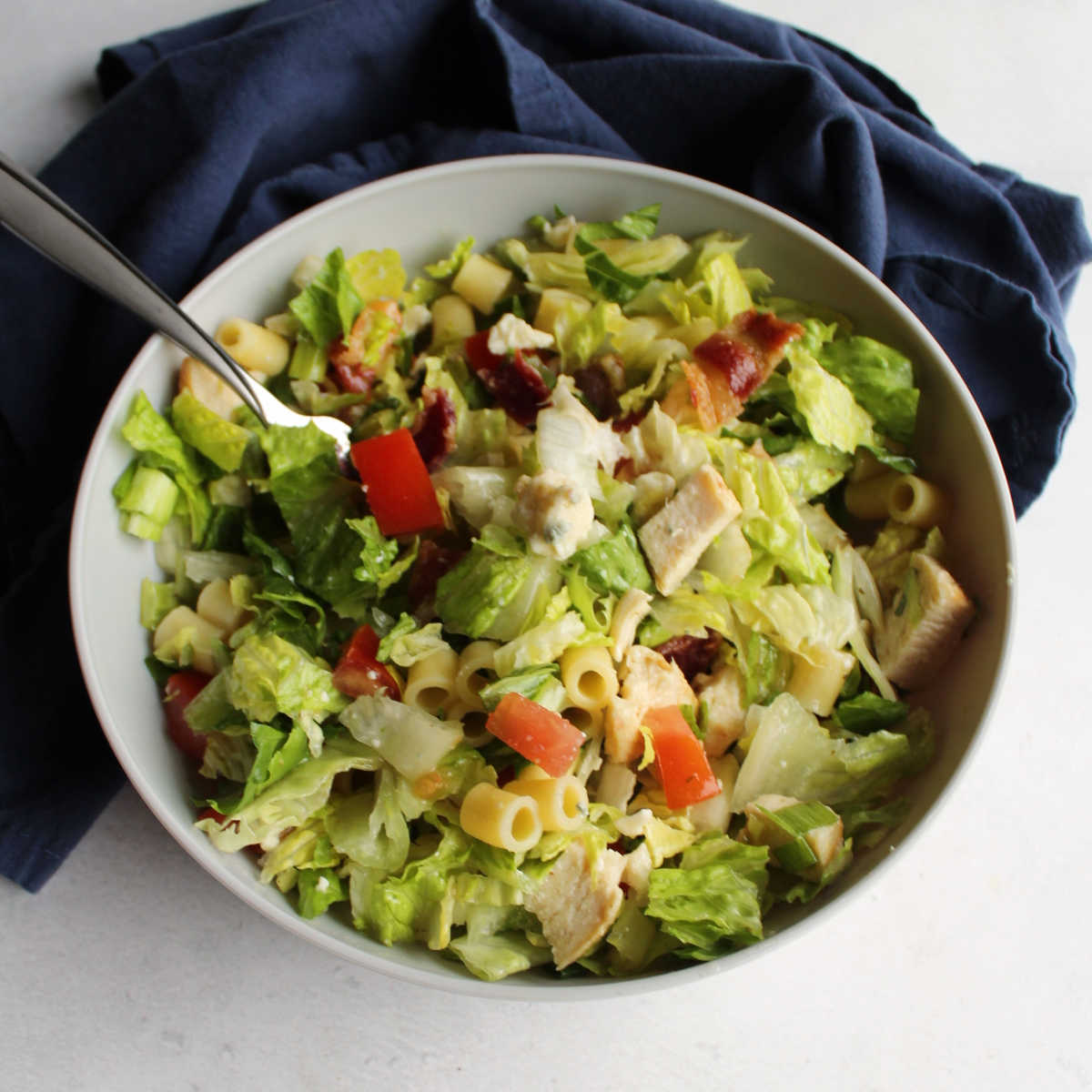 Bowl of portillo's style chopped salad with lettuce, pasta, bacon, tomatoes, chicken, cheese and more.