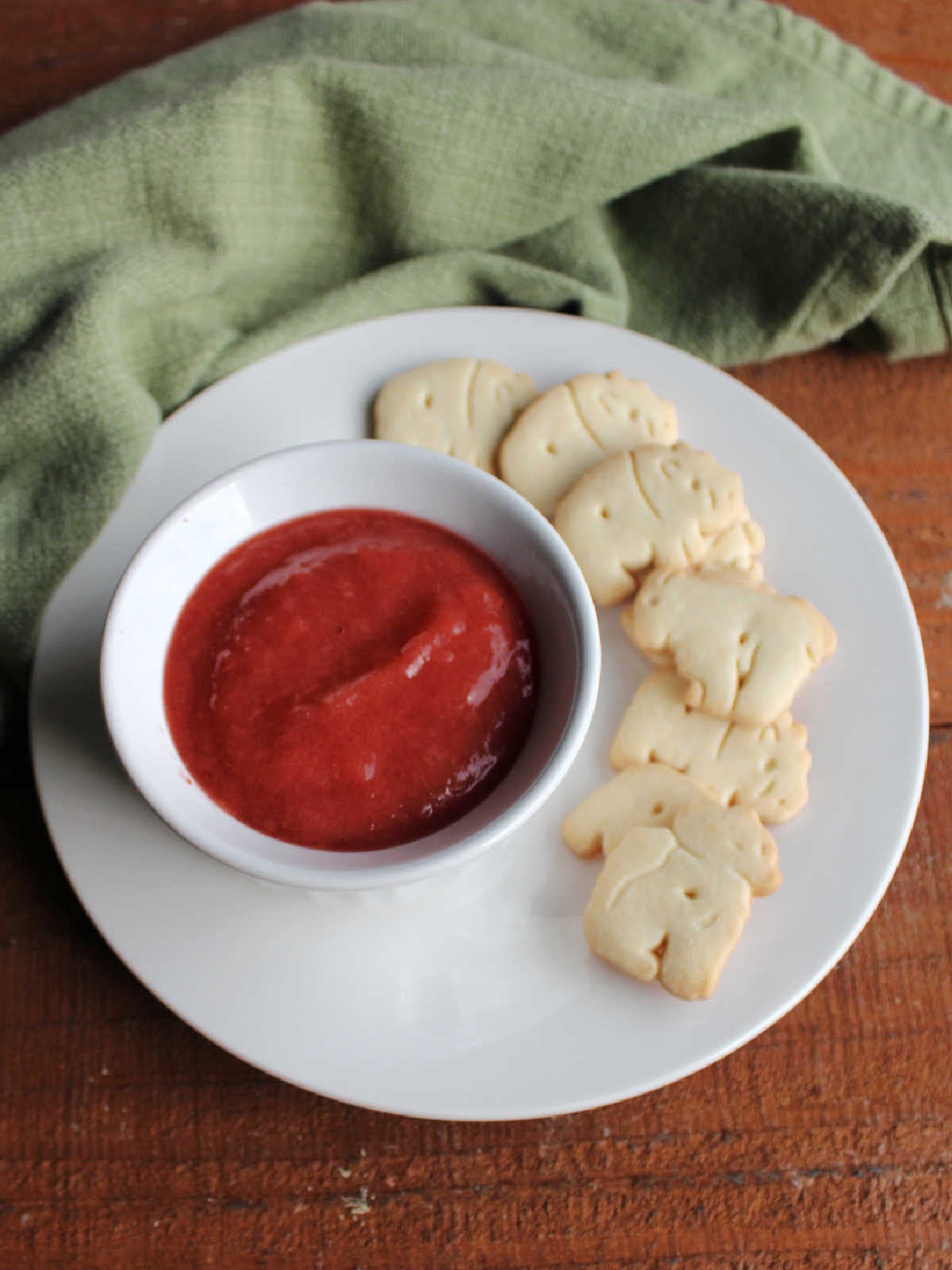 Plate with ramekin of thick strawberry rhubarb sauce with animal cookies nearby.