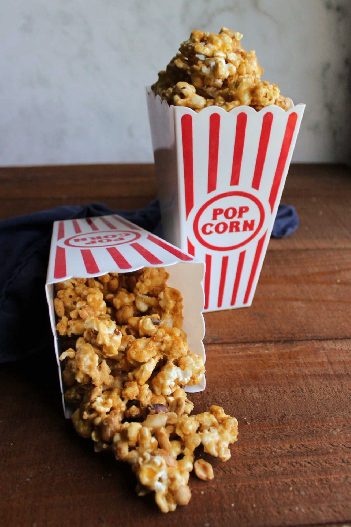 Red and white popcorn containers with caramel coated popcorn, one spilled over.