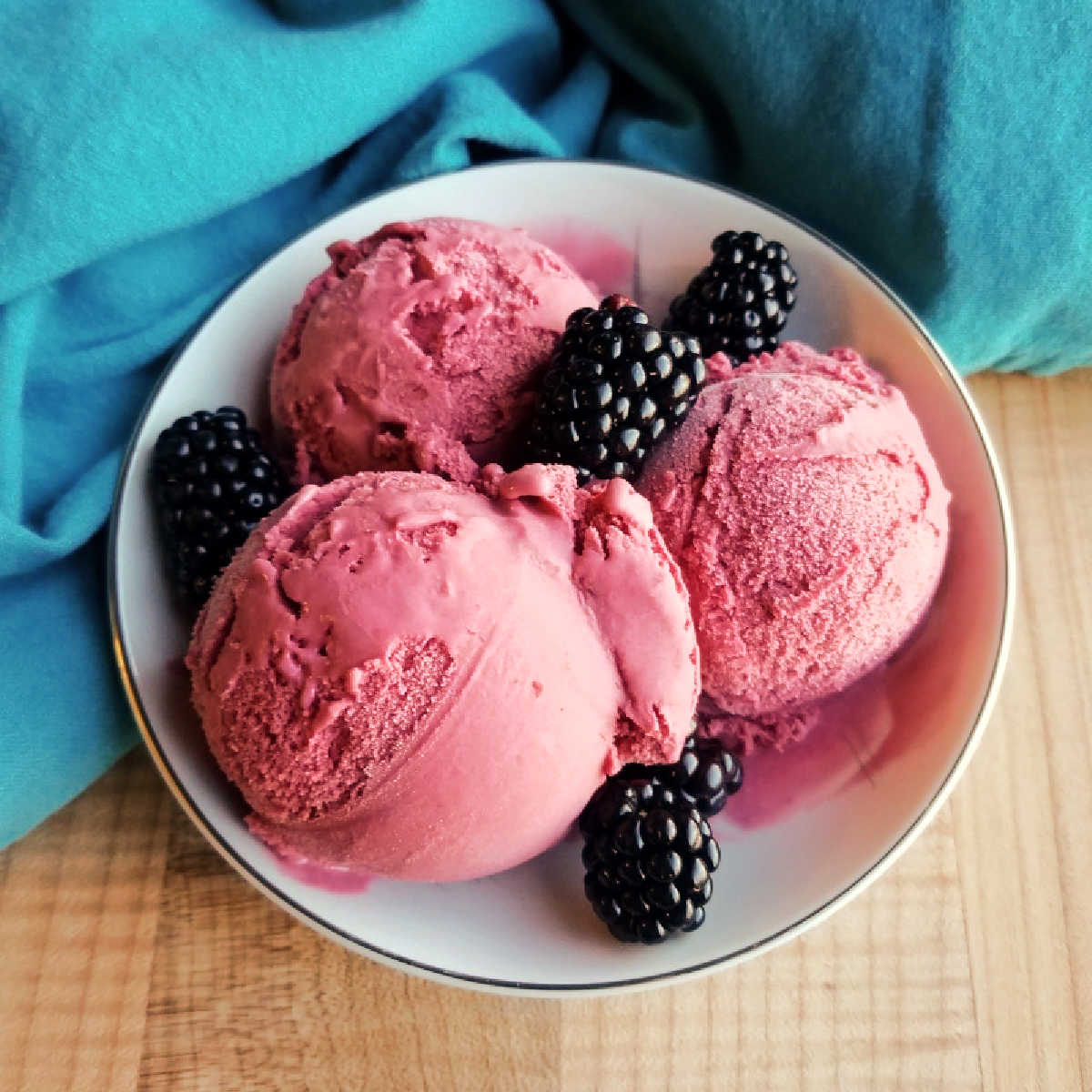 bowl with big beautiful scoops of blackberry ice cream and some fresh blackberries on top.