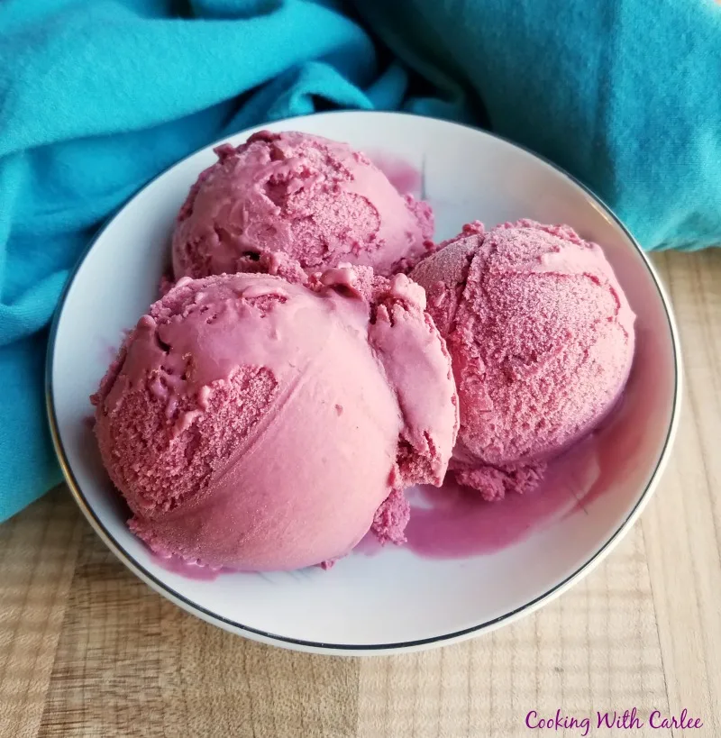 3 big purple scoops of blackberry ice cream in small white bowl.