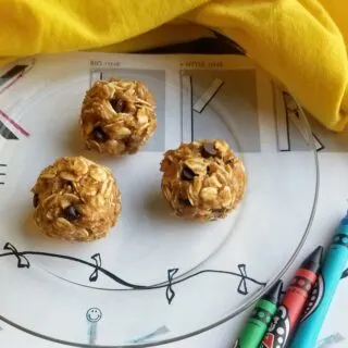 The peanut butter, banana and honey oatmeal balls with chocolate chips on glass plate next to coloring sheet and crayons.