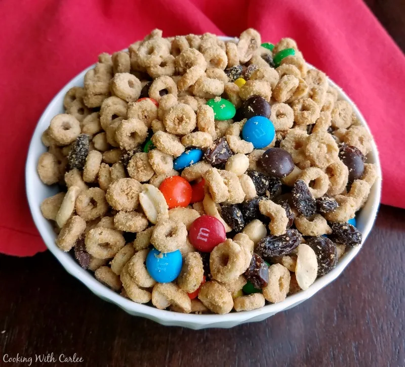 Bowl of snack mix with cheerios and peanut coated in maple peanut butter mixture with raisins and M&Ms. 