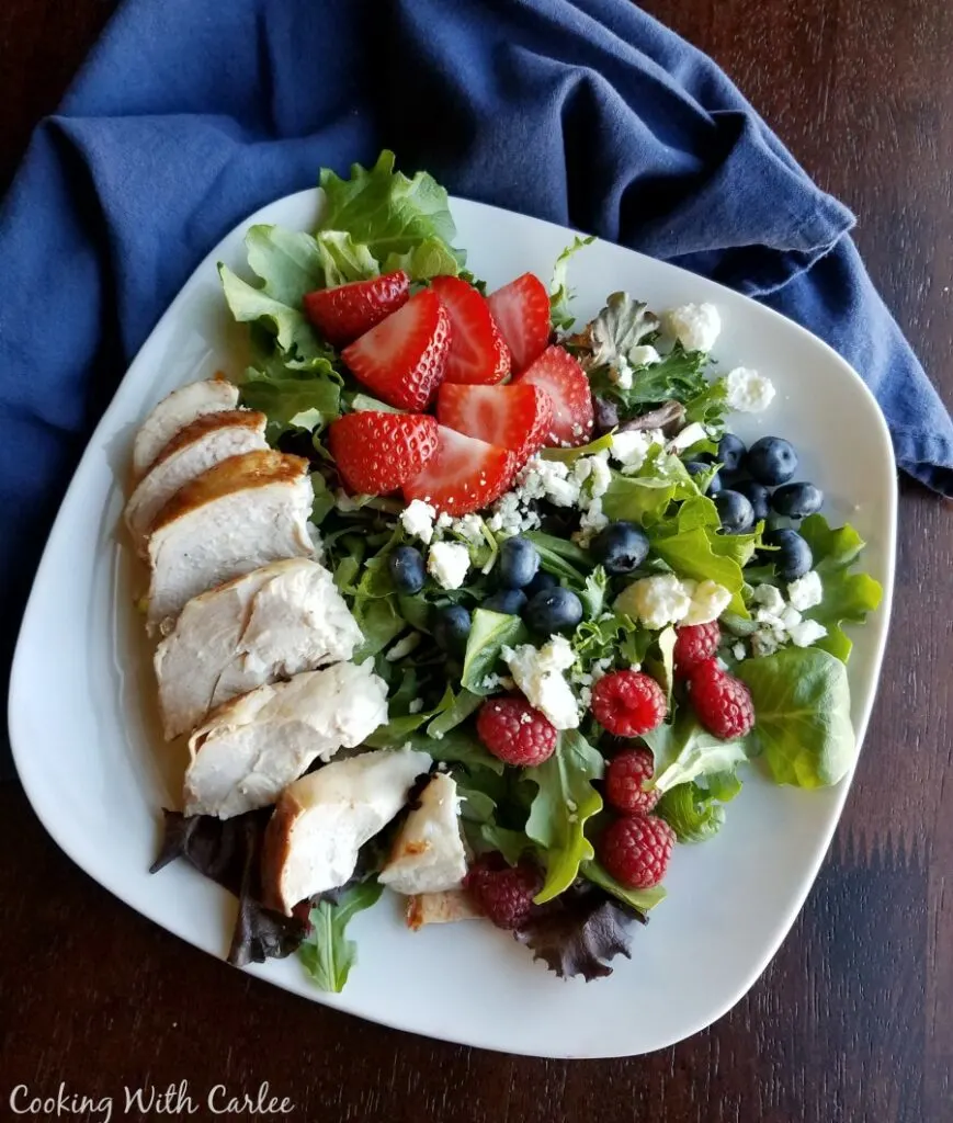 plate of greens with chicken breast, raspberries, strawberries, blueberries and crumbled cheese.