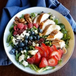 bowl of salad topped with fruit, cheese, nuts and more.