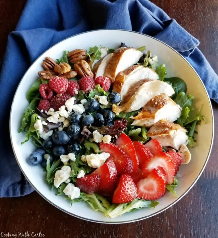 bowl of salad topped with fruit, cheese, nuts and more.