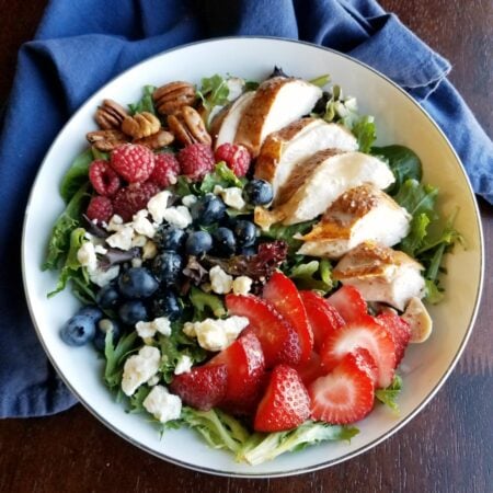 bowl of salad topped with fruit, cheese, nuts and more.