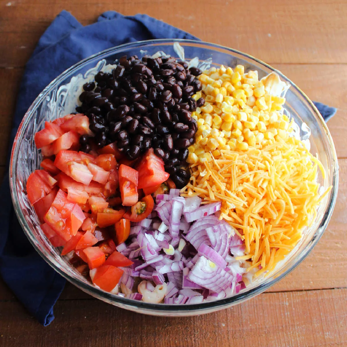 Tomatoes, red onion, cheese, corn and black beans ready to be stirred into the bbq ranch  macaroni salad.