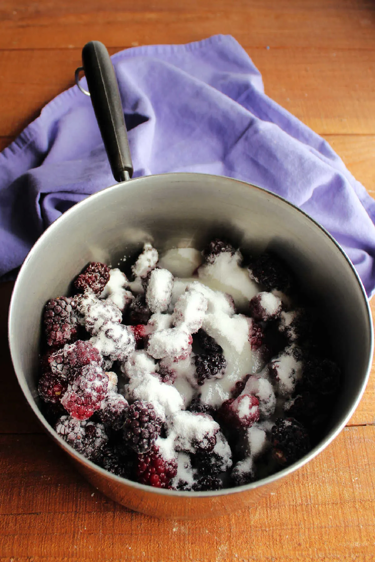 Saucepan filled with frozen blackberries, sugar and lemon juice, ready to cook.