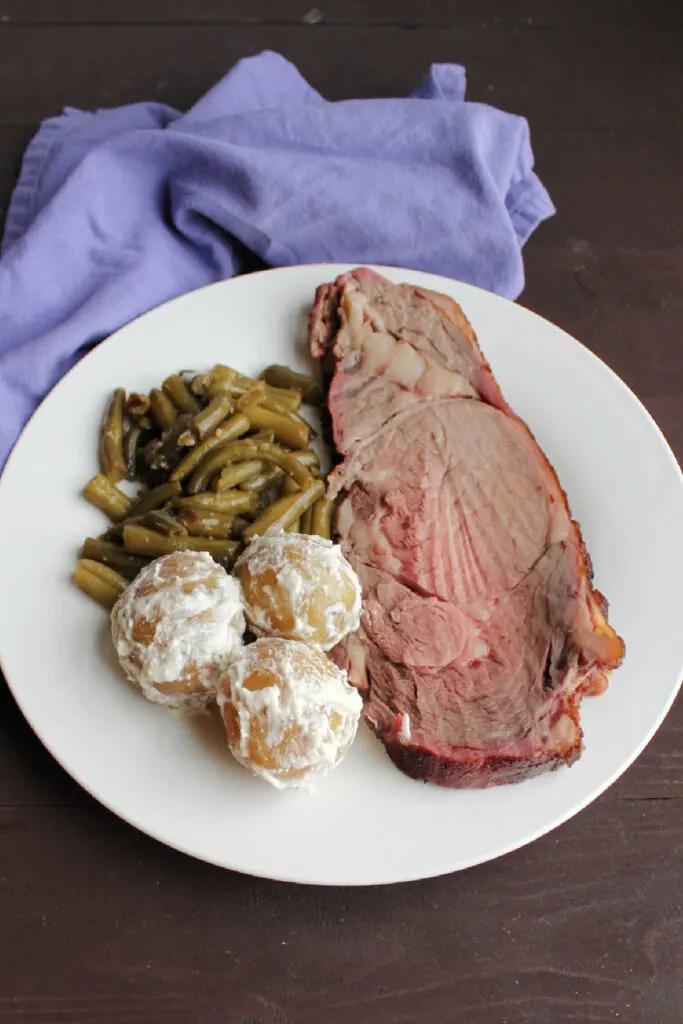 Slice of prime rib, smothered green beans and sour cream and chive coated new potatoes on plate ready to eat.