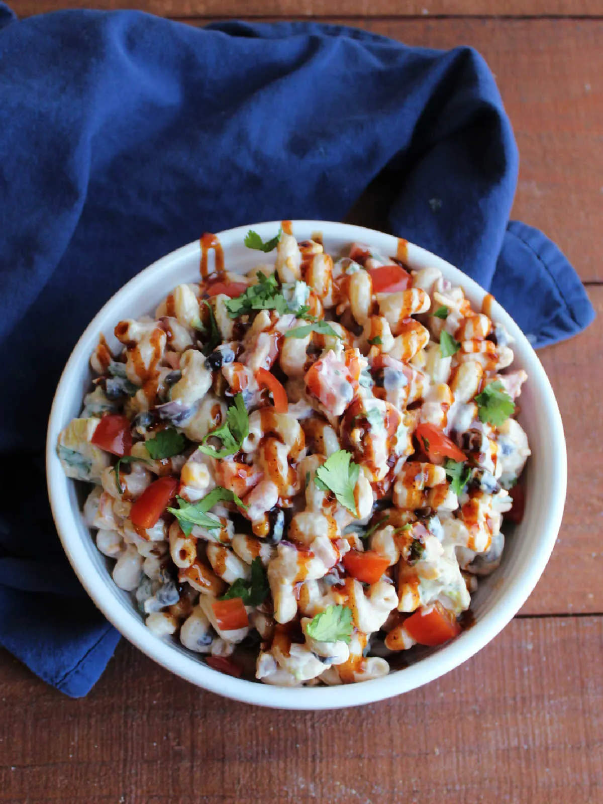 Serving bowl of bbq ranch pasta salad topped with fresh diced tomato, cilantro and a drizzle of bbq sauce. 