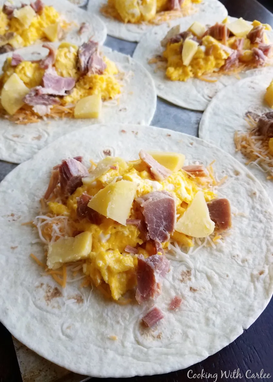 tortillas tipped with scrambled eggs, ham and chunks of cooked potato ready to be rolled into chimichangas.