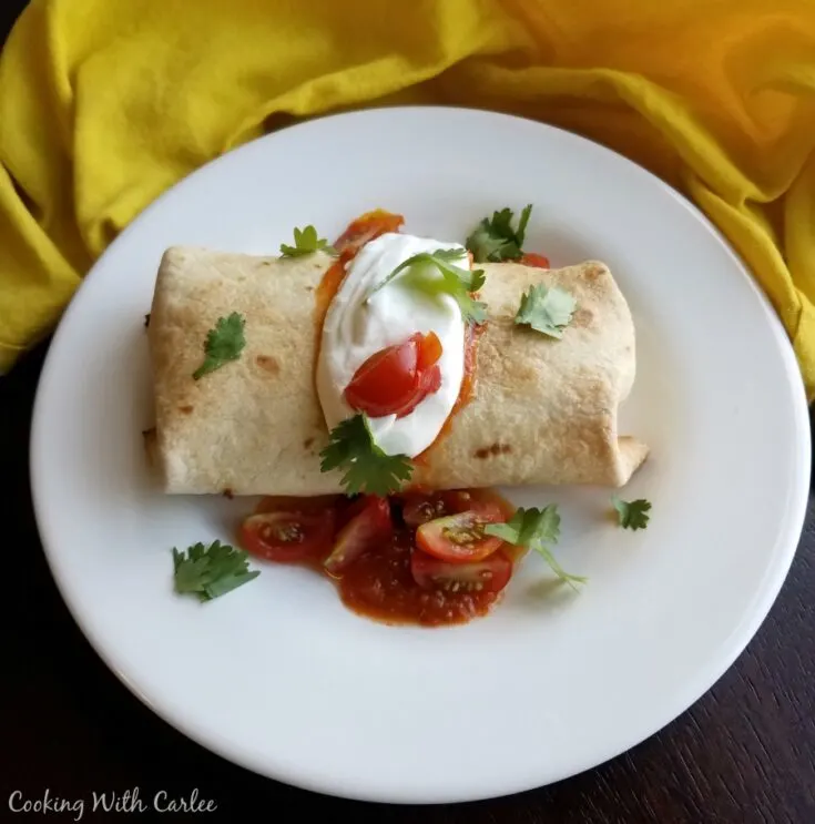 Baked breakfast chimichanga with sour cream, tomatoes and cilantro on top.