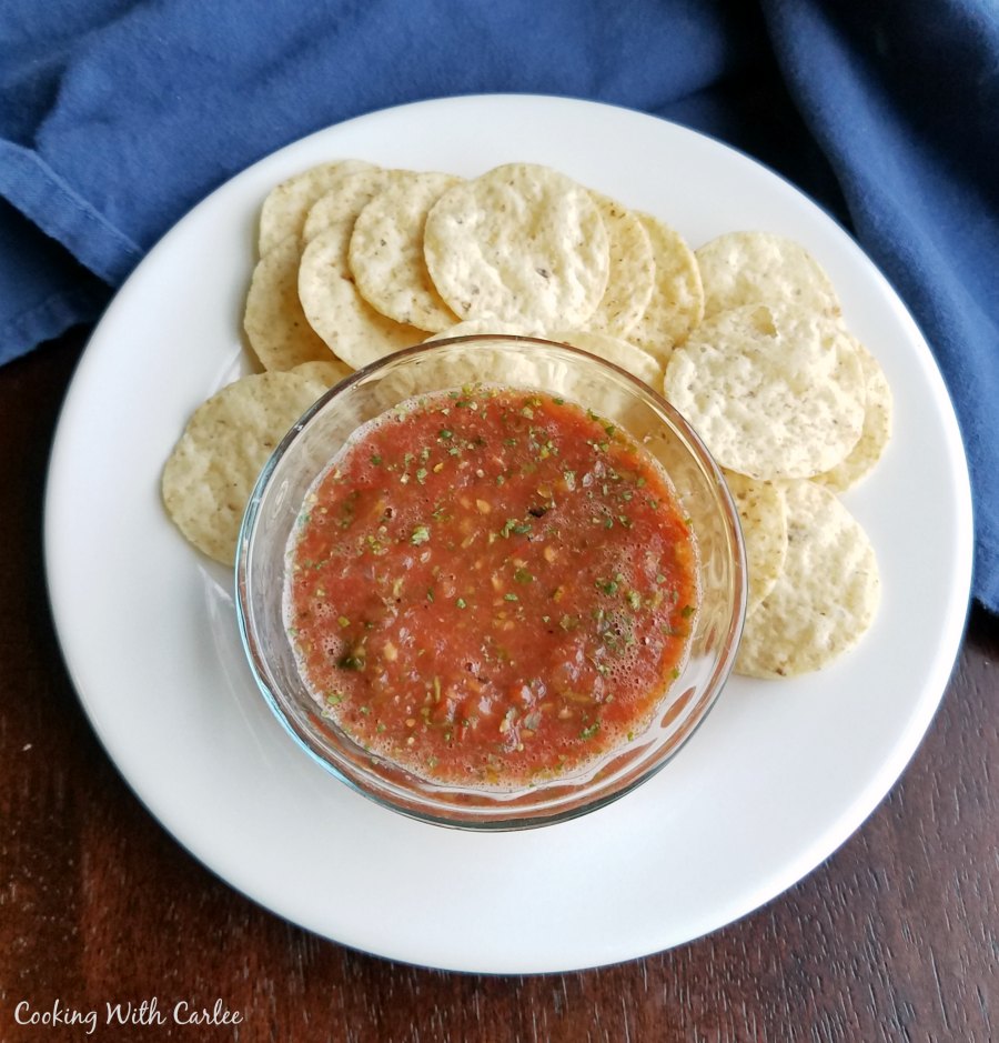 bowl of salsa on plate with chips.