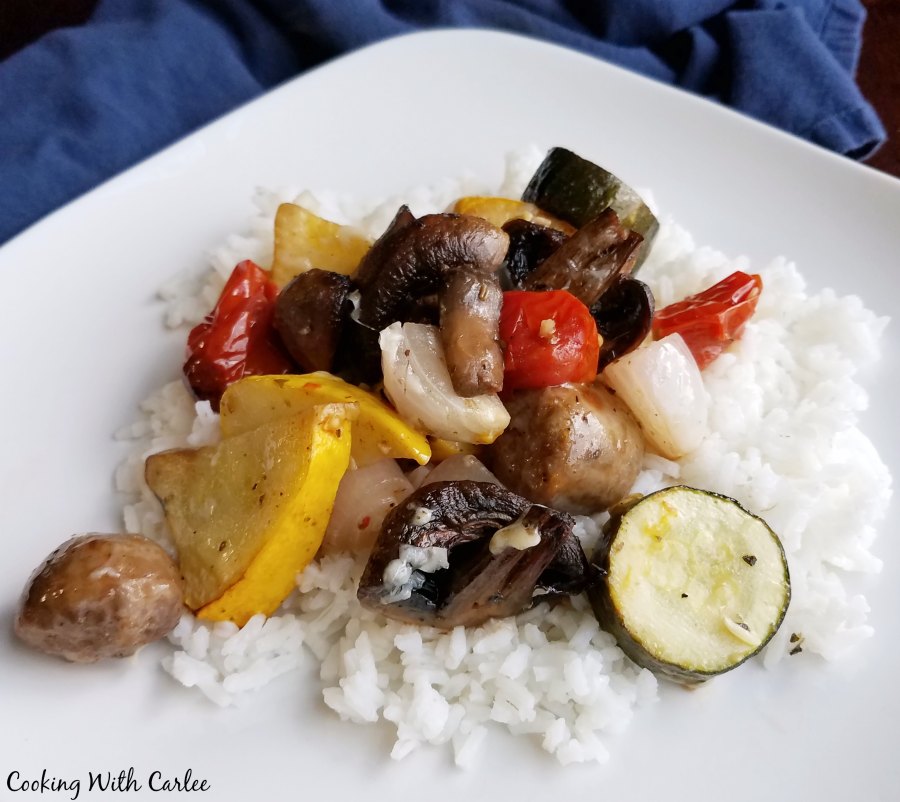 Plate of rice topped with roasted summer vegetables and Italian sausage ready to eat. 