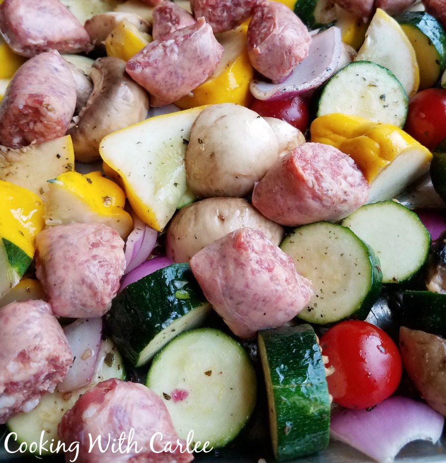 Sheet pan filled with marinated vegetables and Italian sausage, ready to cook.