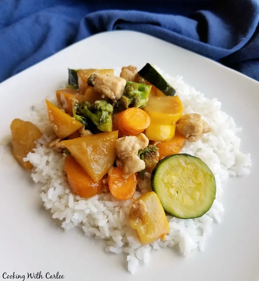 Dinner plate with stir fried chicken and vegetables in light sauce served over a bed of rice.
