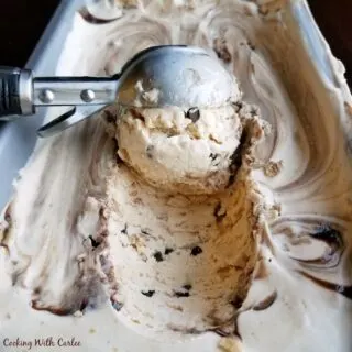 Scooping out a scoop of sundae ice cream with chocolate chips, chocolate swirl, bits of sugar cone, and caramel inside.