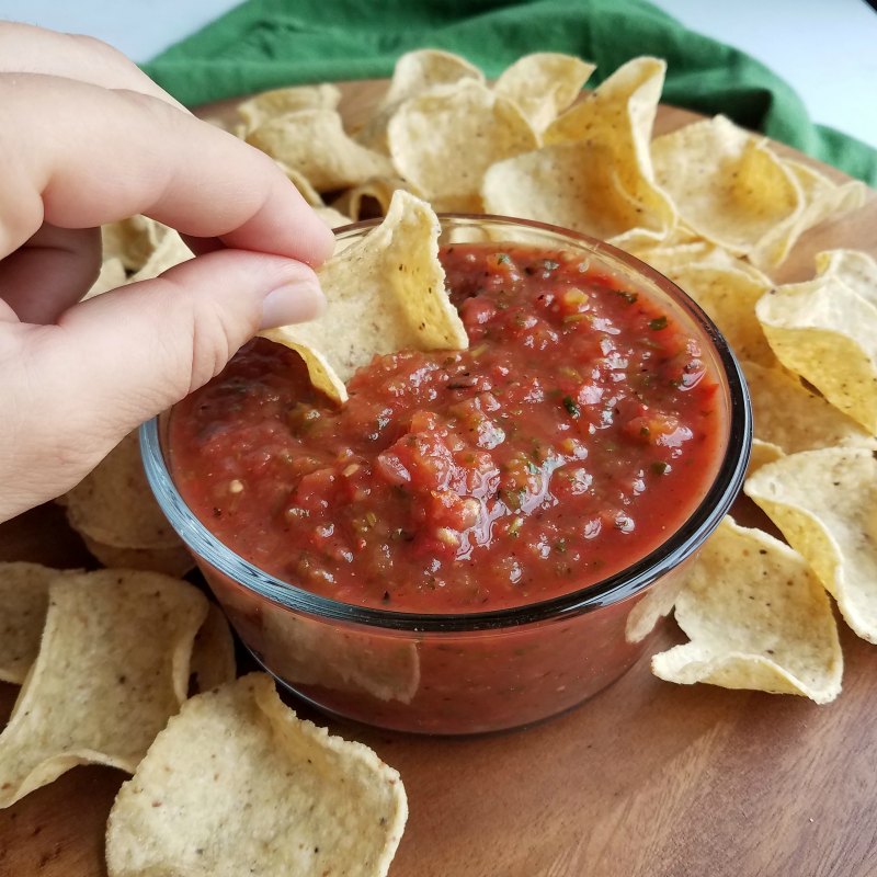 hand dipping tortilla chip into bowl of fresh roasted salsa.