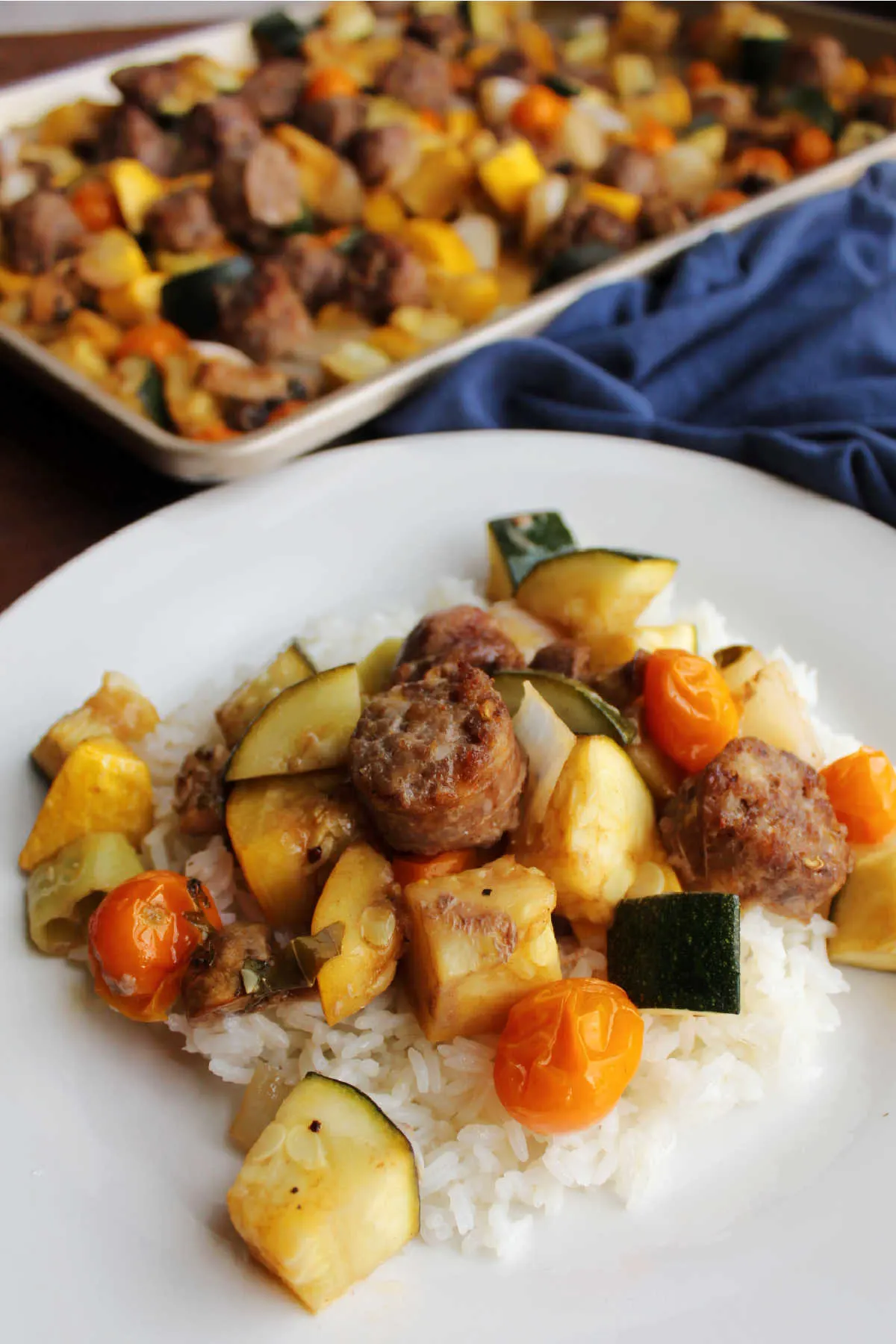 Close up of Italian sausage and vegetables served over rice with sheet pan of remaining sausage and veggies in the background. 