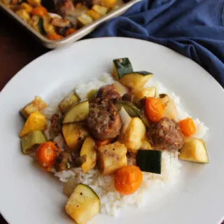 Dinner plate of sausage and vegetable sheet pan meal served over rice with remaining sausage and veggies in sheet pan in the background.