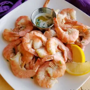 plate piled high with key lime roasted shrimp, a small container of lime butter for dipping and a couple of lemon wedges.