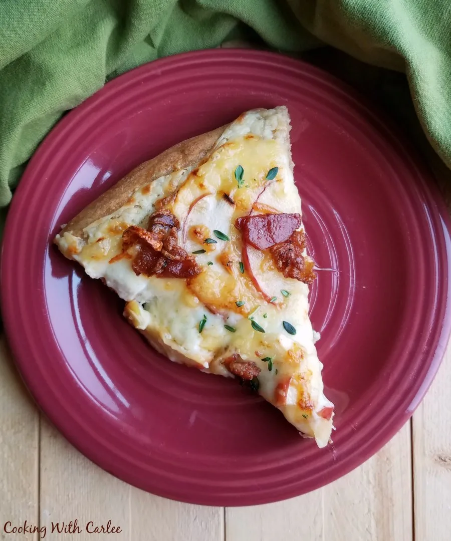 slice of apple bacon pizza with white sauce on plate.