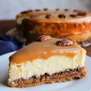 Slice of caramel pecan cheesecake with a layer of caramel and pecans under the cheesecake and another layer of caramel and pecan halves on top.