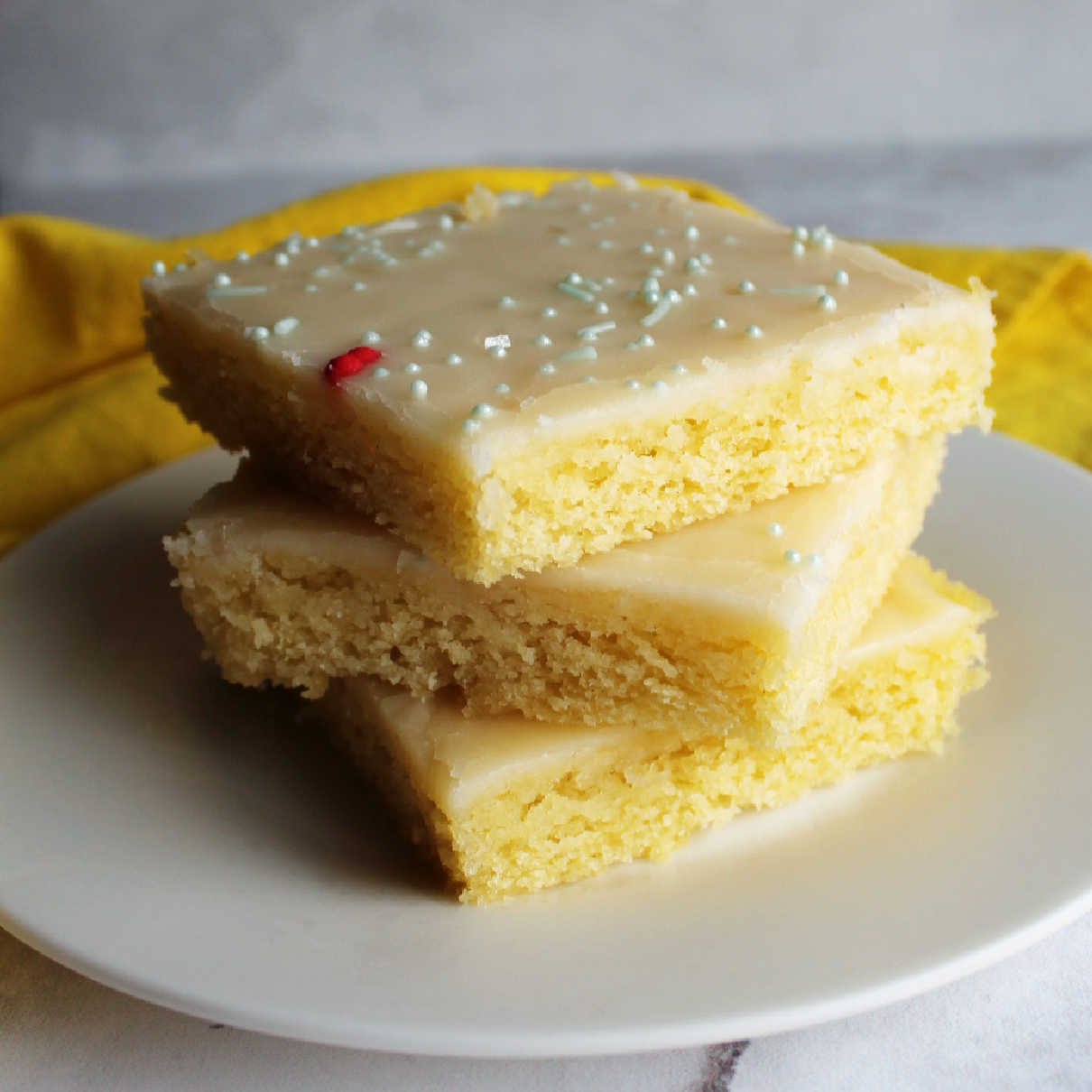 Stack of slices of lemon Texas sheet cake with smooth icing and sprinkles on top.